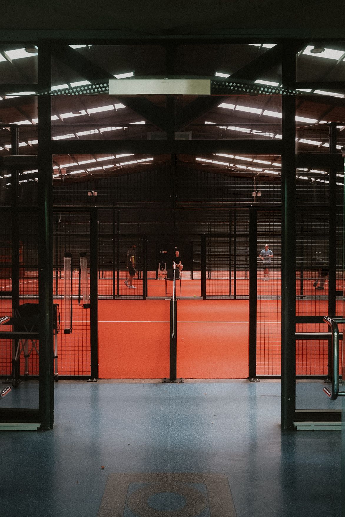 Indoor padel and pickleball courts with players on a red court